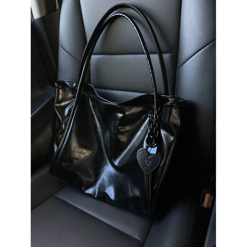Black Patent Leather Handbag with Heart Charm on Gray Leather Seat | Luxury Fashion Bag