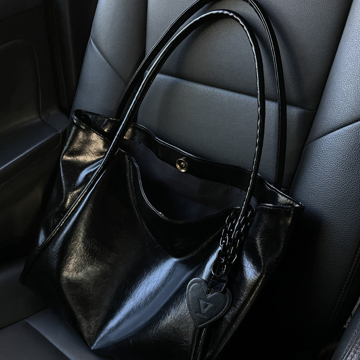 Black Patent Leather Handbag with Heart Charm on Gray Leather Seat | Luxury Fashion Bag