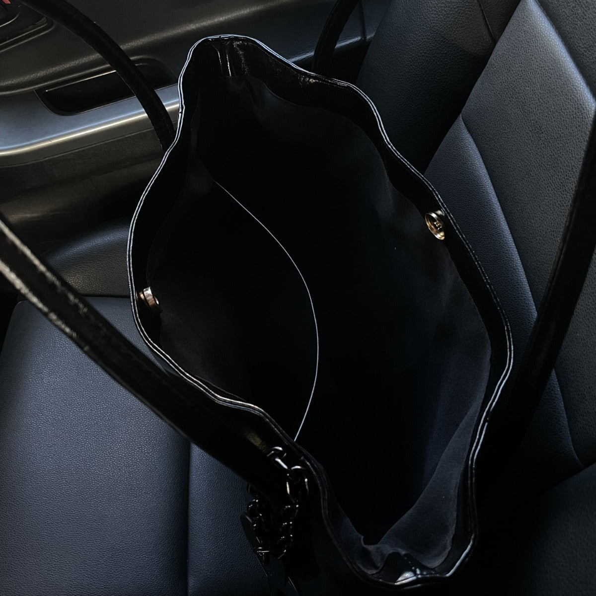 Black Patent Leather Handbag with Heart Charm on Gray Leather Seat | Luxury Fashion Bag