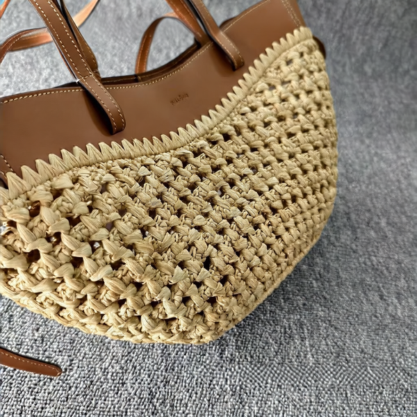 Natural raffia open-weave crochet woven large tote bag with smooth tan cognac leather side panels, contrast white topstitching and structured flat leather top handles, close-up detail shot on grey textured surface showing intricate knotted basket weave texture