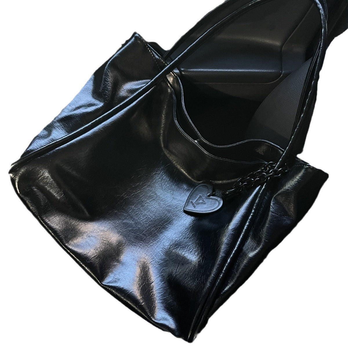 Schwarze Lacklederhandtasche mit Herzanhänger auf grauem Ledersitz | Luxuriöse Modetasche 