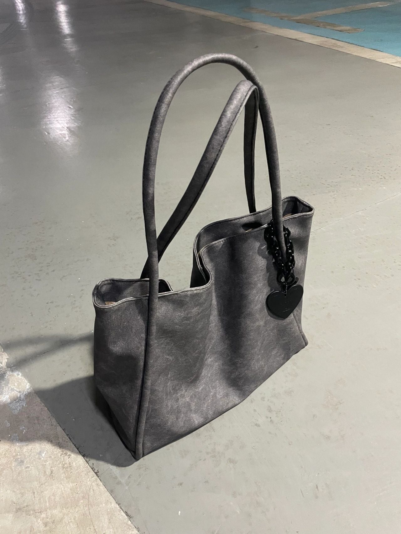 Schwarze Lacklederhandtasche mit Herzanhänger auf grauem Ledersitz | Luxuriöse Modetasche 